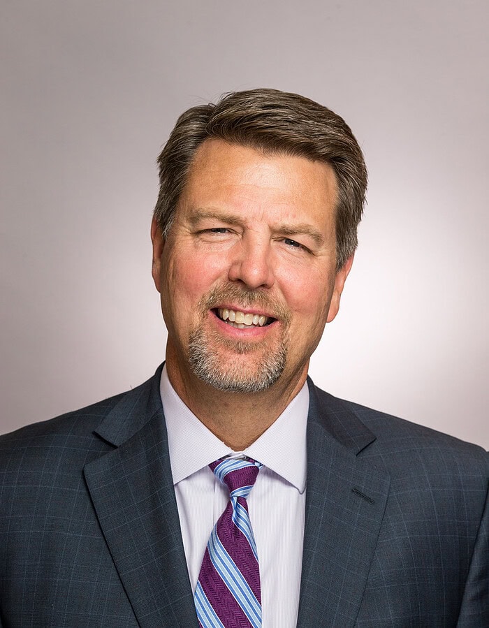 Male business professional in a dark suit and purple striped tie photographed in studio.