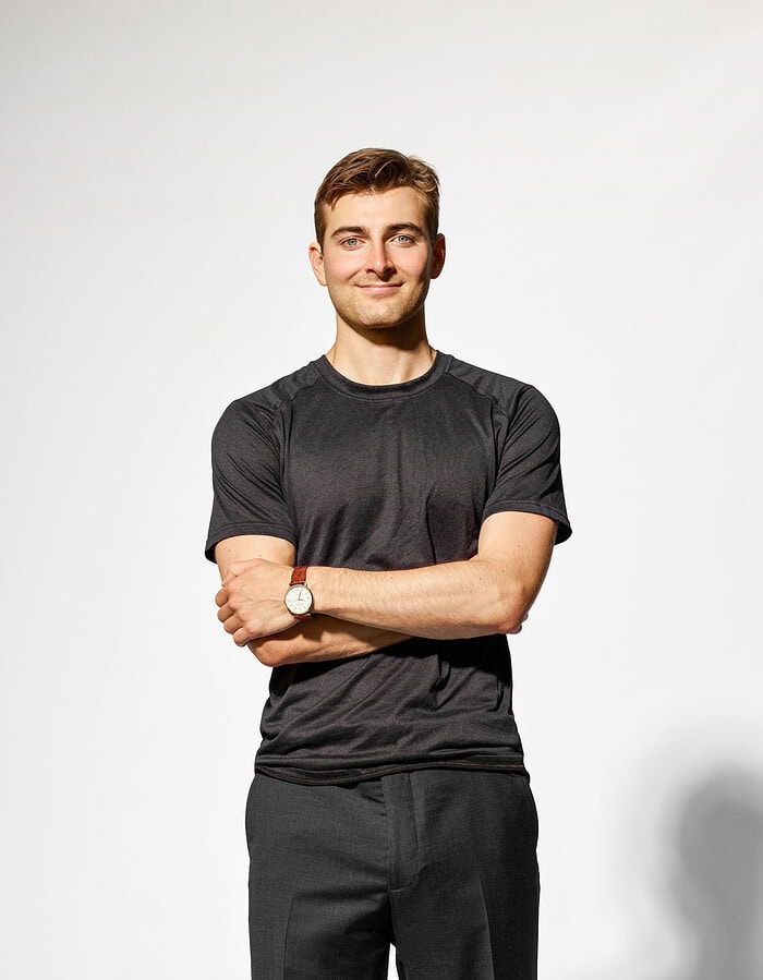 Young male professional in a black T-shirt standing with his arms crossed in a white studio.