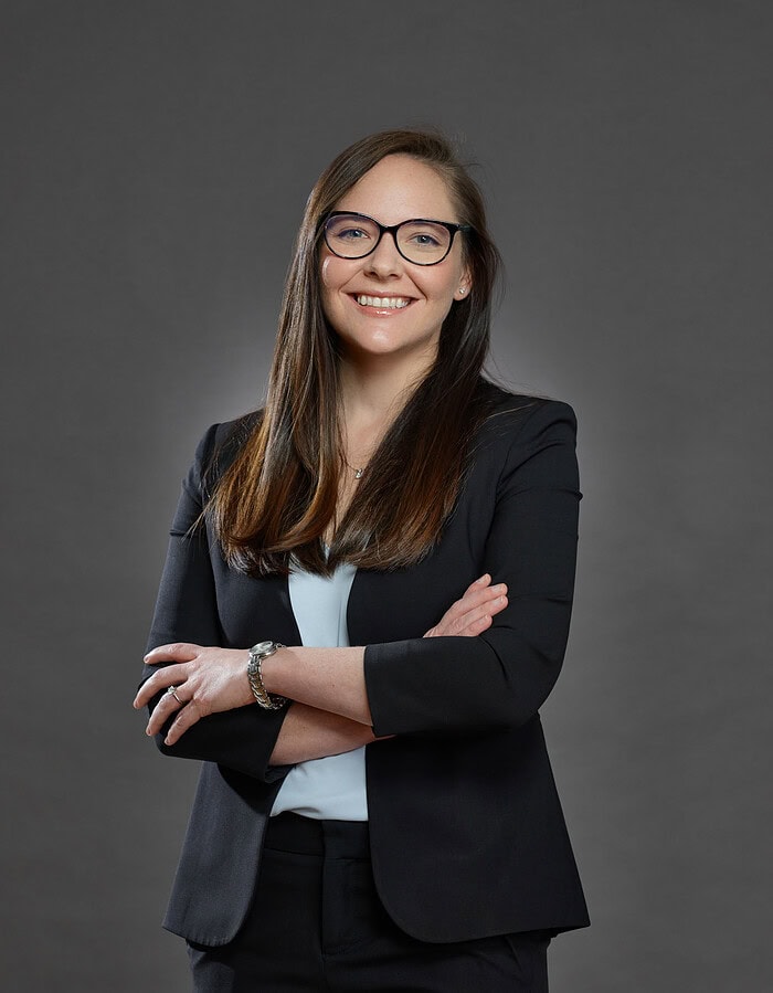 Female corporate professional wearing glasses and a dark blazer with her arms crossed.