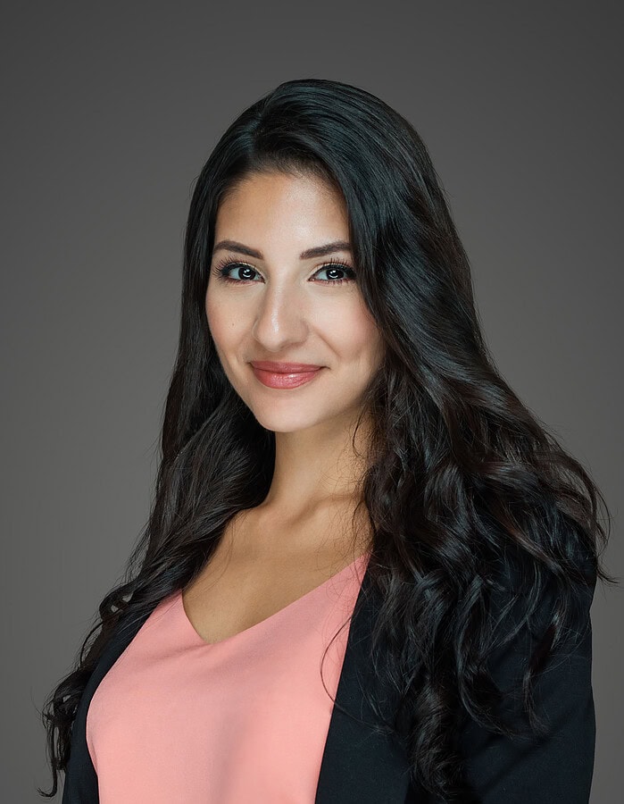 Female professional with long dark hair wearing a black blazer and soft pink blouse.