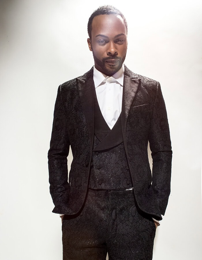Actor Jaz Anderson wearing a black patterned three-piece suit in a studio editorial portrait.