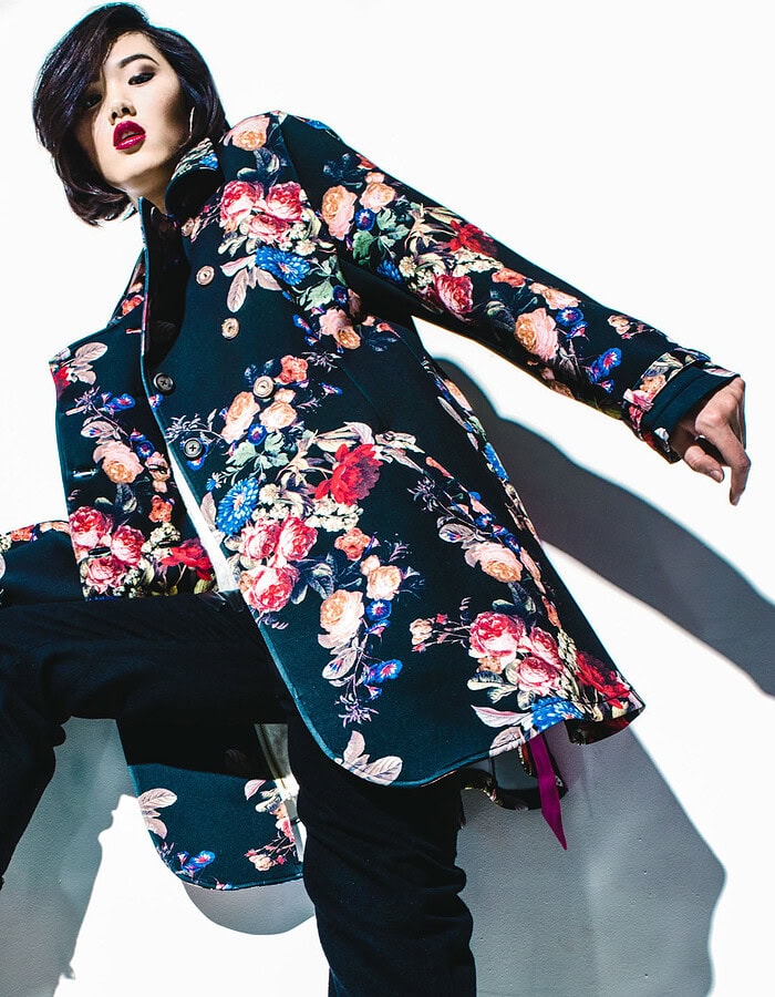 Low-angle portrait of a model wearing a dark floral coat with black cropped trousers and ankle boots.