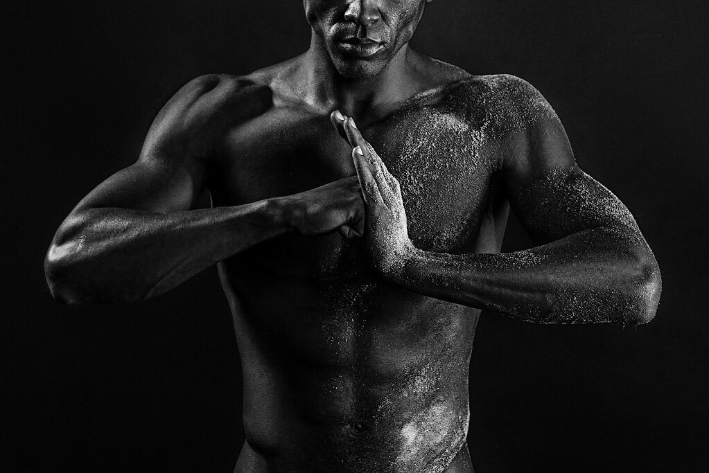 Study Cropped black-and-white portrait of a male model pressing his hands together across a sand-textured torso.