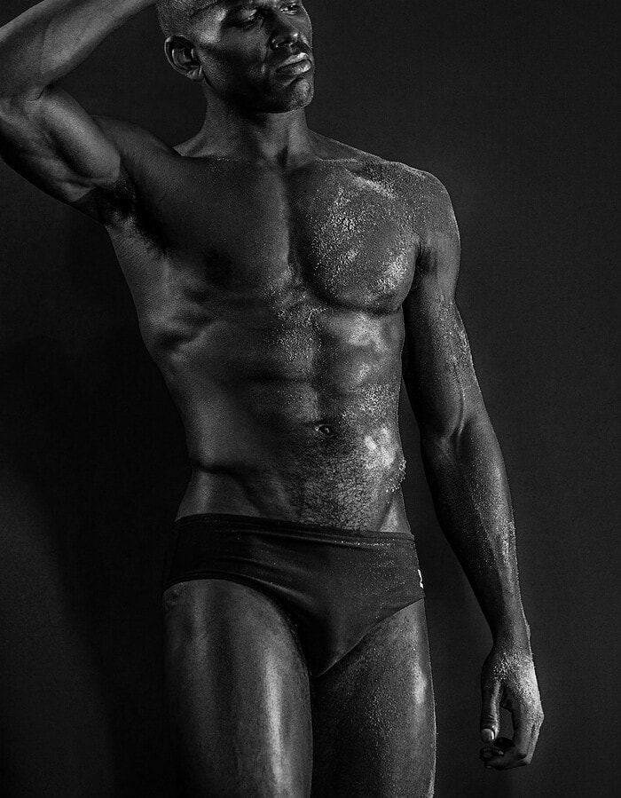 Male model posing with one arm raised in a black-and-white studio body study