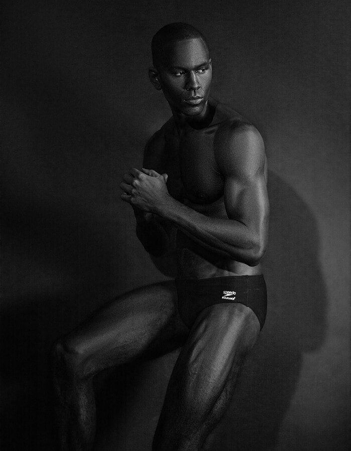 Male model seated with clasped hands in a dark monochrome studio portrait