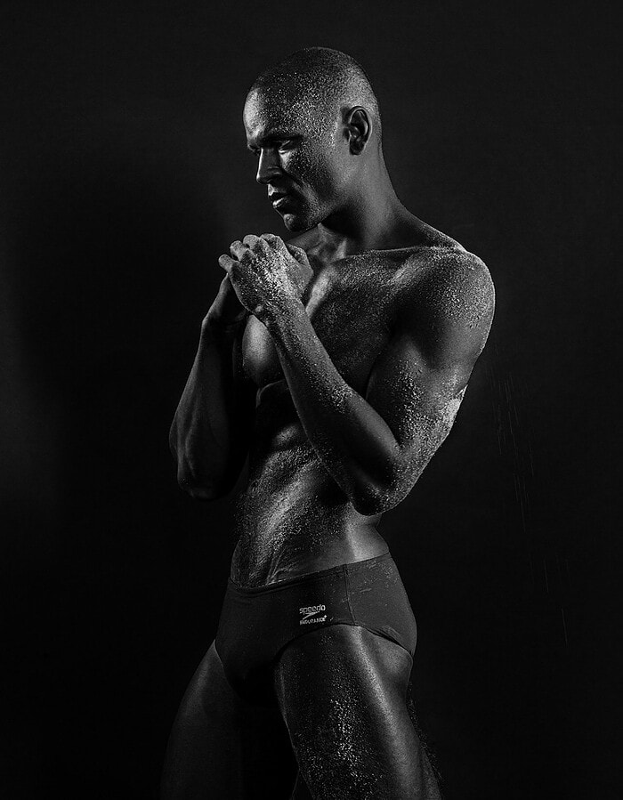 Standing male model with hands clasped in a textured black-and-white portrait