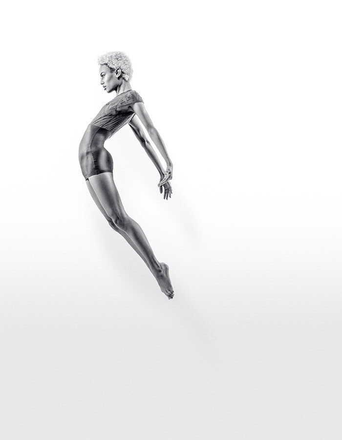 Full-length dancer floating in midair against a white studio background