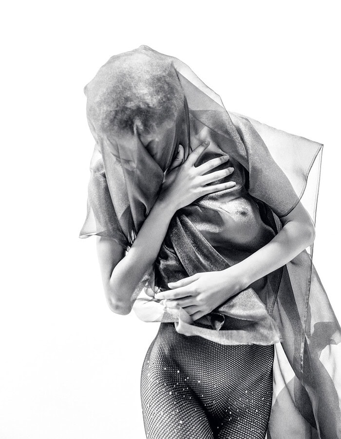 Dancer bending forward beneath translucent fabric in a monochrome studio portrait