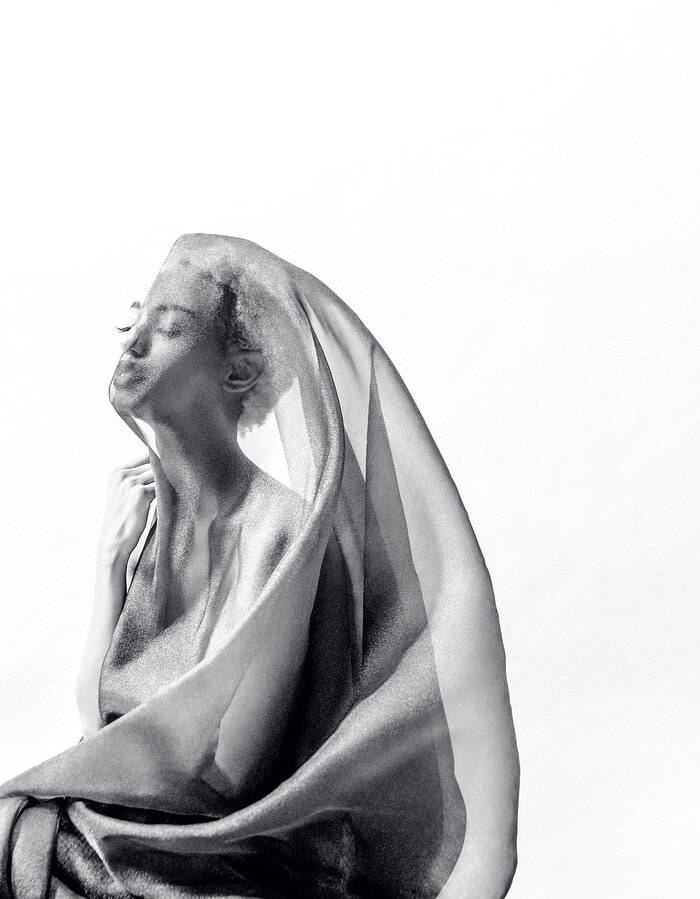 Profile of a dancer beneath translucent fabric against a white background