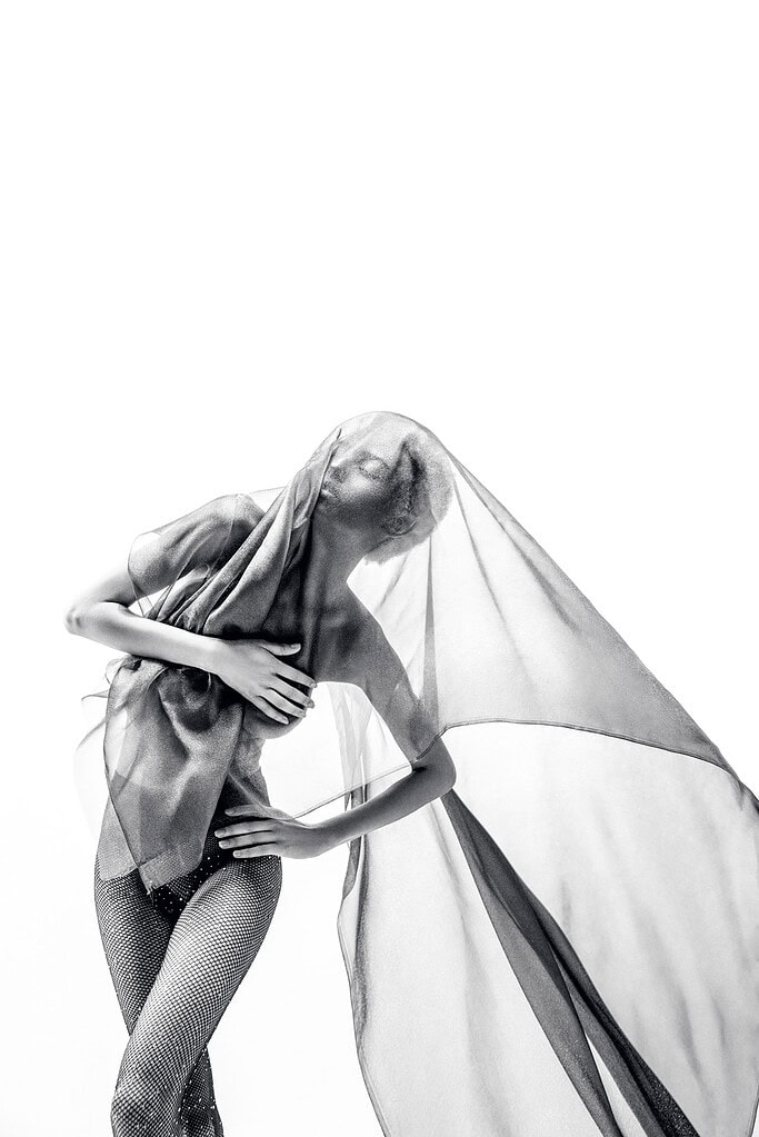 Dancer leaning sideways as translucent fabric extends through the frame