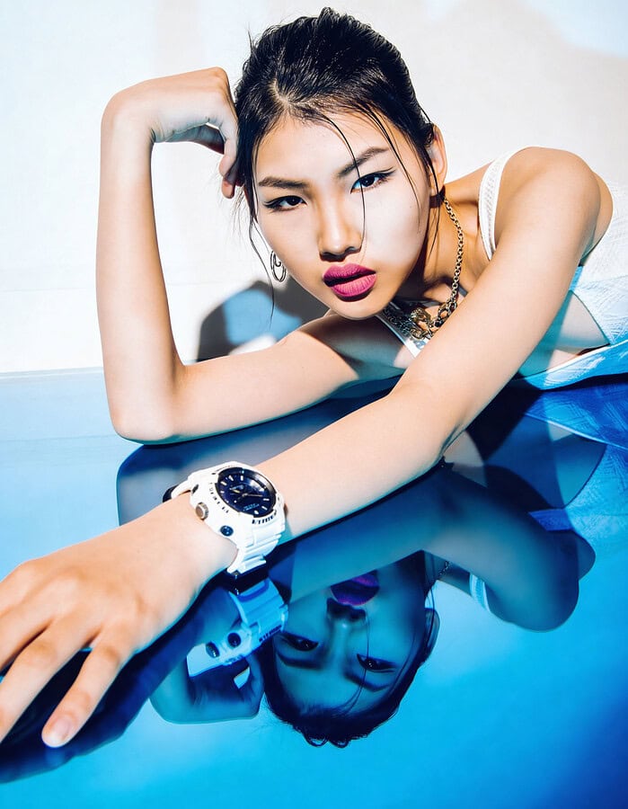 Close beauty portrait of a fashion model reflected in a glossy blue surface, wearing a white watch and pink