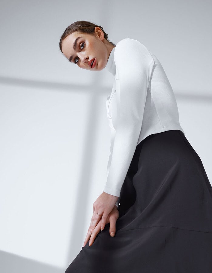 Low-angle fashion portrait of a model in a white fitted top and sculptural black skirt.