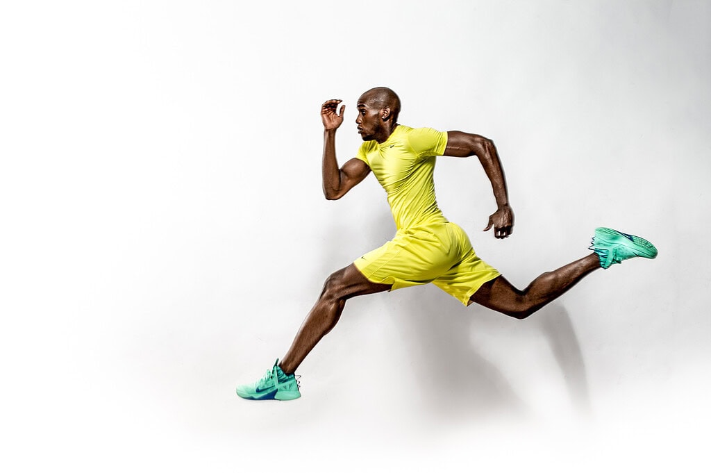 Athletic male model airborne in a running pose wearing yellow sportswear and mint-green sneakers.