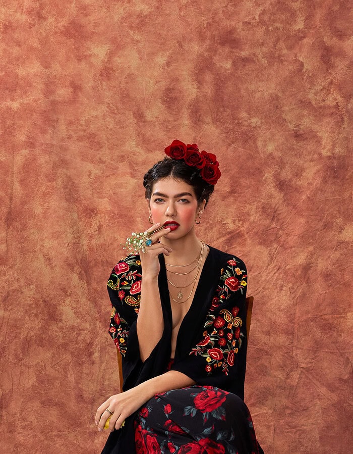 Woman in a black embroidered garment seated with small white flowers held near her lips.