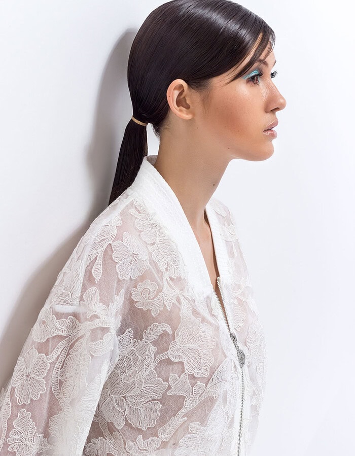 Profile beauty portrait of a model in a white floral lace jacket with turquoise eye makeup.