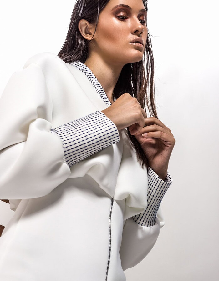 Low-angle beauty portrait of a model with wet hair wearing a white dress with blue-patterned trim.