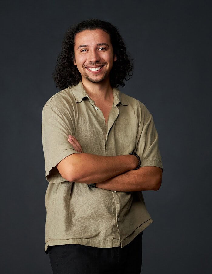 Casual studio portrait of a smiling man with long curly hair and folded arms.