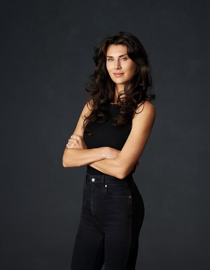 Confident studio portrait of a dark-haired woman in black with folded arms.