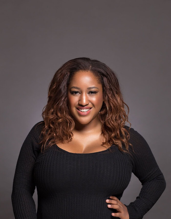 Confident personal portrait of a smiling woman in black against a neutral studio background.