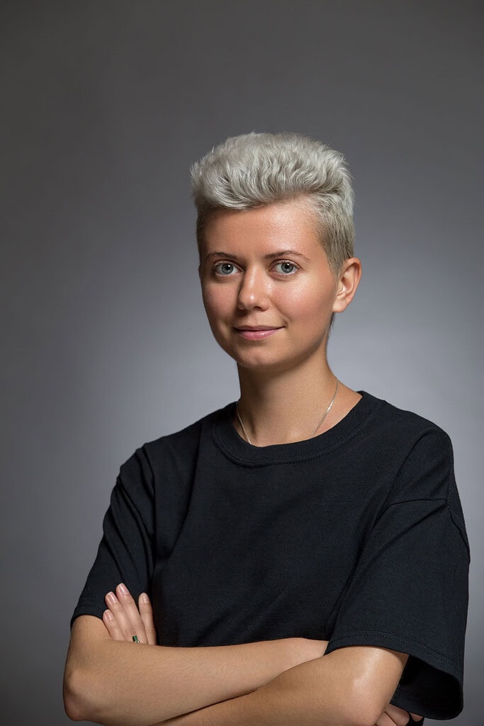Contemporary studio portrait of a person with short silver hair wearing a black shirt.