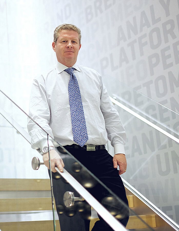 Corporate executive standing on a modern staircase beside a suspended metal sculpture.