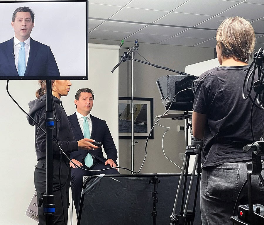 Man in a suit being filmed for a corporate interview, with a monitor and camera operator in the foreground.