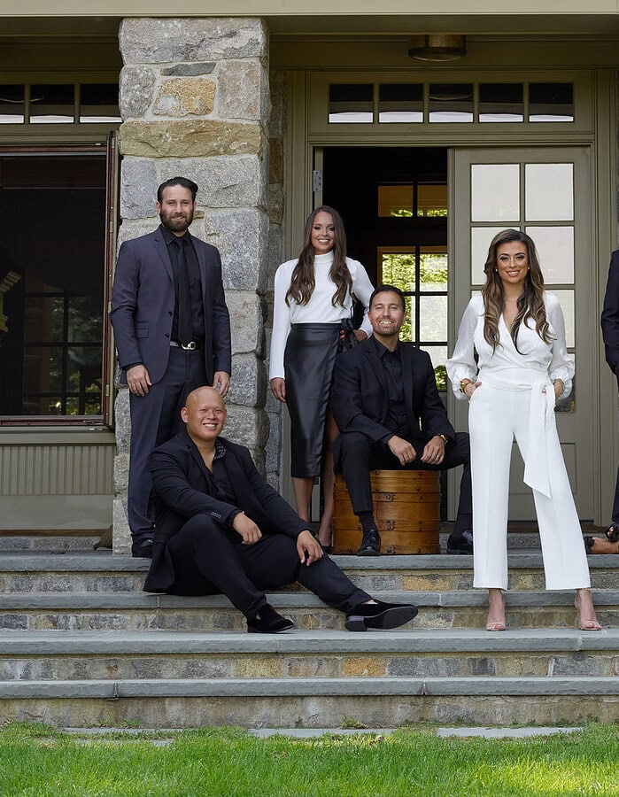 Corporate team dressed in black and white posed on the stone steps of a residential property.