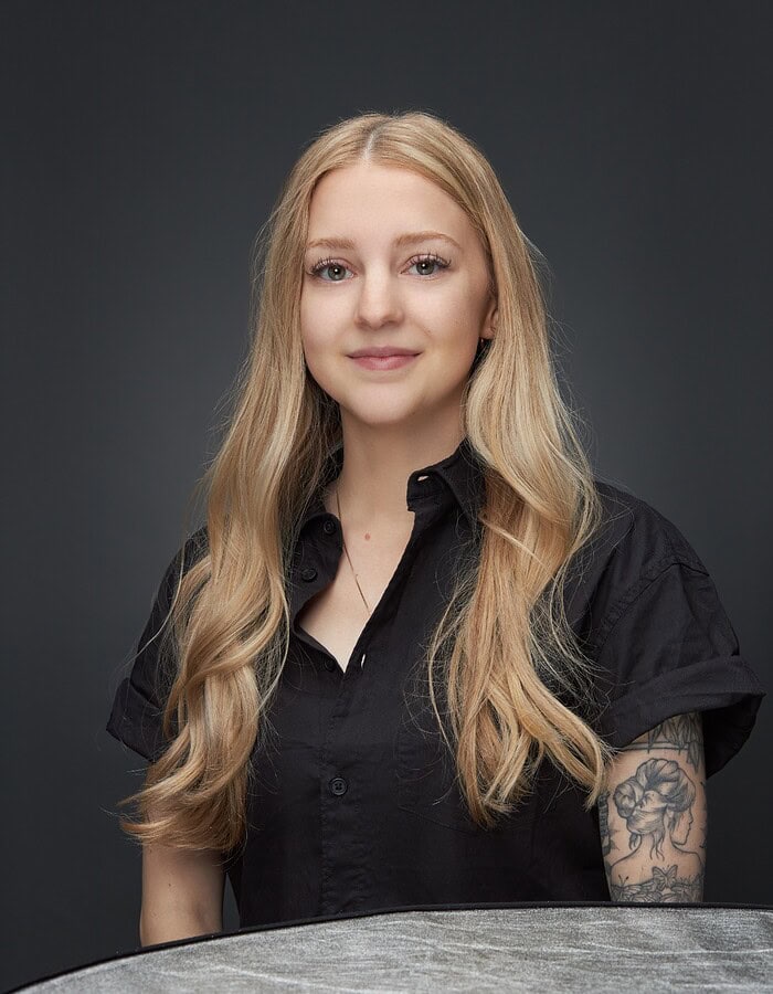 Studio portrait of a blonde creative professional in a black shirt against a charcoal background.