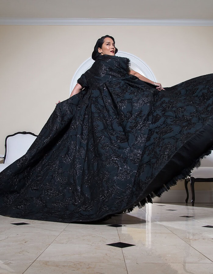 Editorial portrait of a woman twirling a dramatic black gown inside a large elegant room.