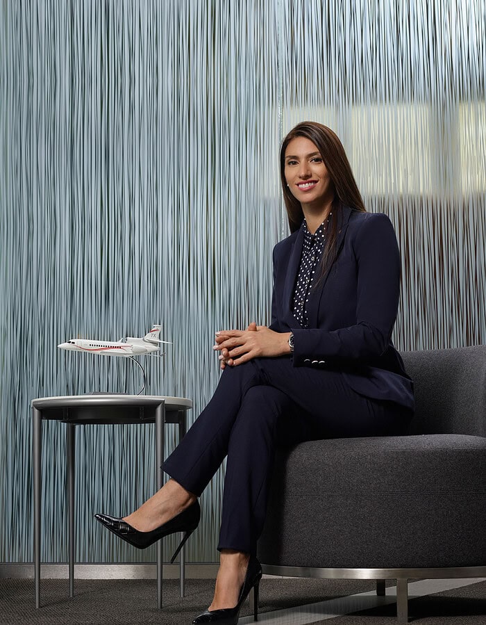 Woman executive seated beside a scale business jet in a contemporary corporate interior.