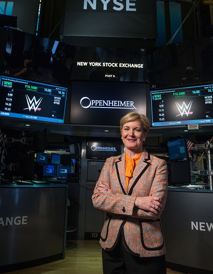 Woman executive standing on the New York Stock Exchange trading floor beneath NYSE and Oppenheimer signage.