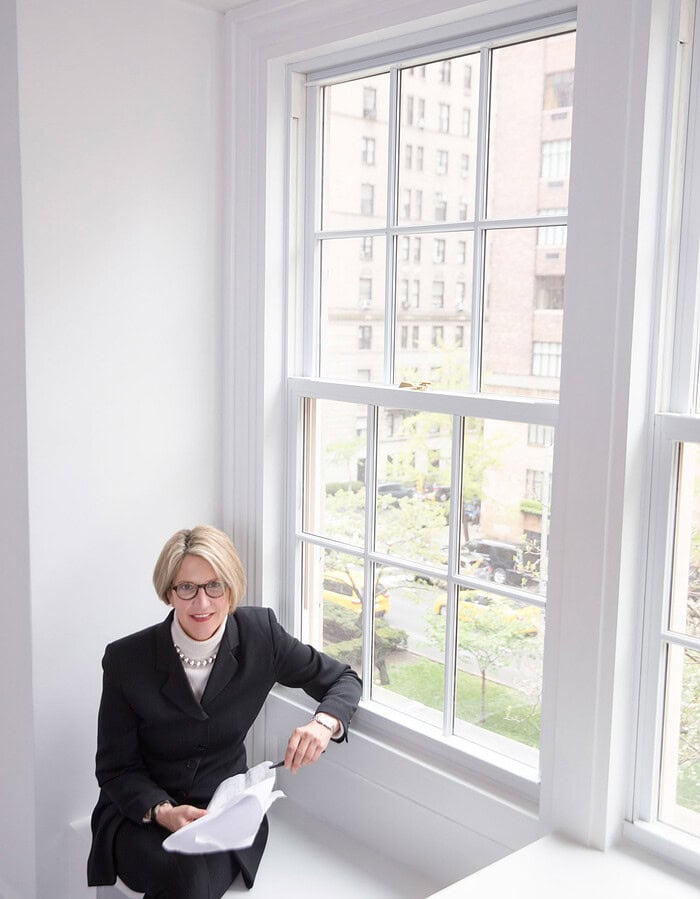 Woman executive seated beside a large office window overlooking a New York street.