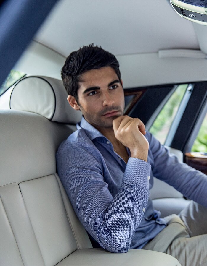 Lifestyle portrait of a man seated inside a luxury car, wearing a blue shirt and looking toward the camera.