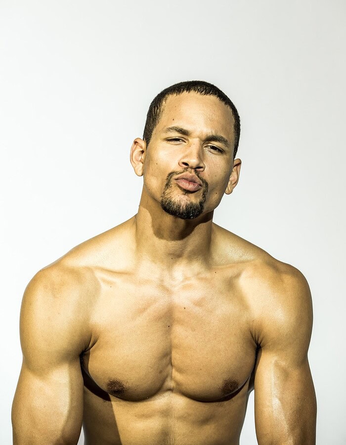 Close portrait of a shirtless male model with a goatee posed against a light gray studio background.