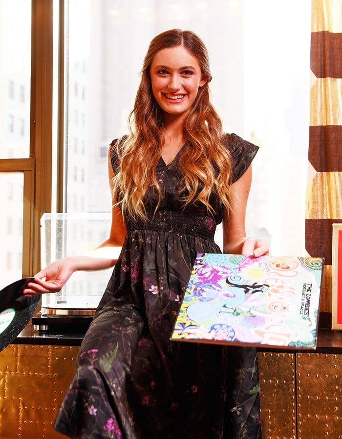 Music artist holding illustrated album artwork in a bright apartment portrait.