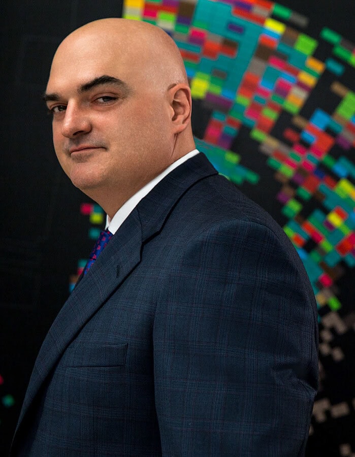 Executive in a dark suit photographed beside a colorful digital art installation in a corporate interior.