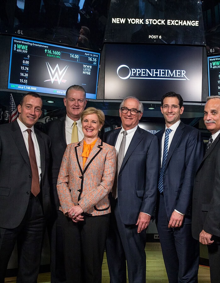 Corporate group photographed on the New York Stock Exchange floor beneath Oppenheimer and NYSE displays.