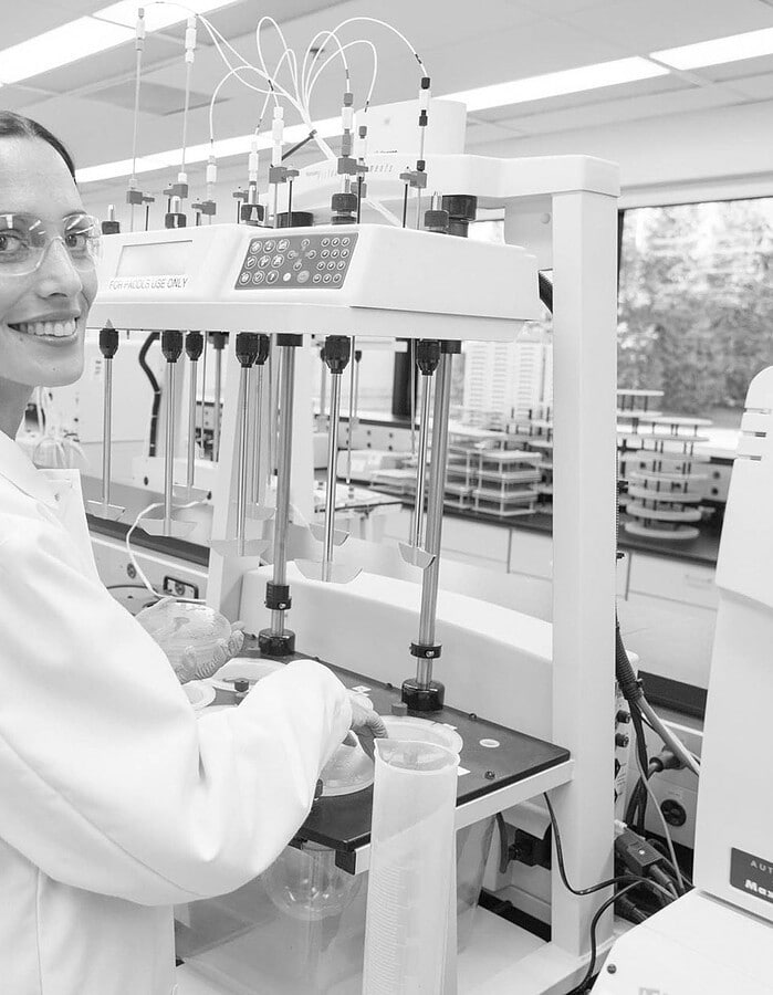 Smiling scientist operating automated laboratory equipment while wearing safety glasses.