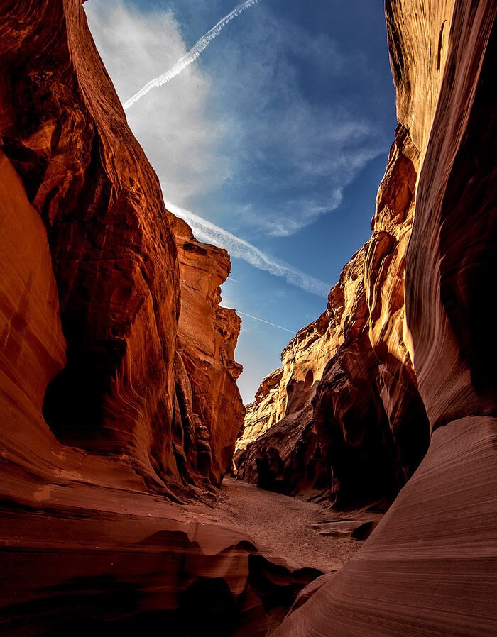 Narrow Antelope Canyon passage with red sandstone walls rising toward blue sky.