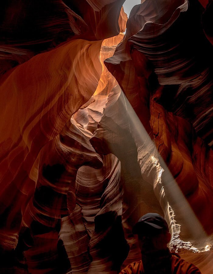 A shaft of sunlight cuts through Antelope Canyon near a guide in silhouette.