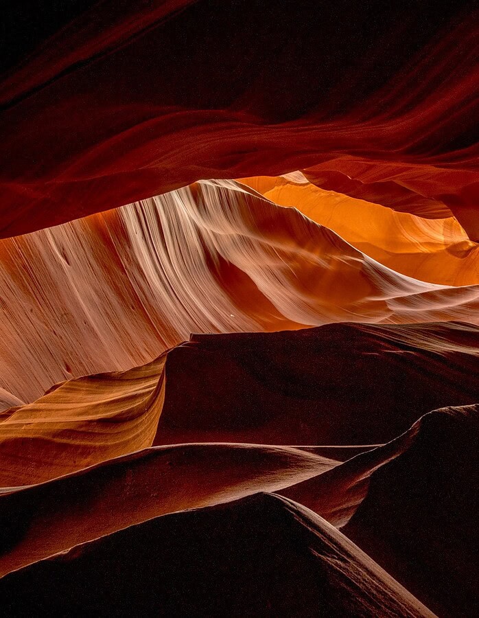 Undulating sandstone rock forms and dark red shadows inside Antelope Canyon.