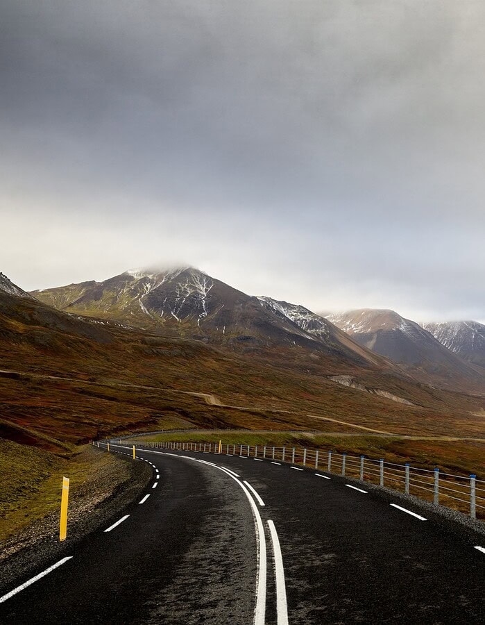 Curving Iceland road leading through a mountain valley toward the coast under low clouds.