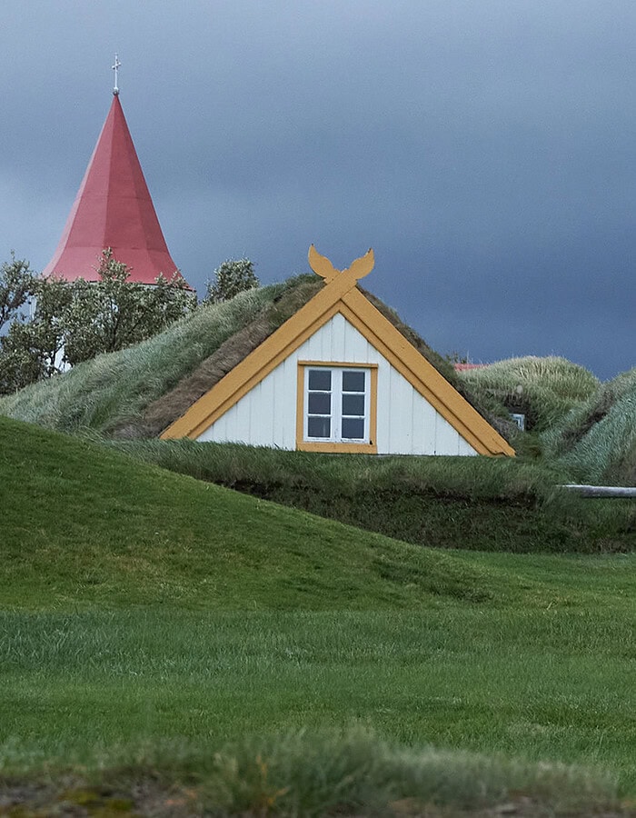 Traditional Icelandic turf houses with yellow trim under dark storm clouds.