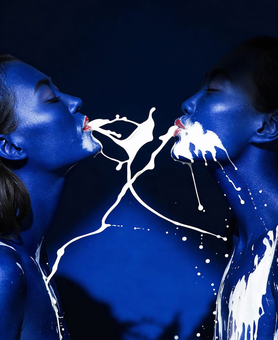 Close conceptual portrait of two models in blue body paint with white liquid motion.