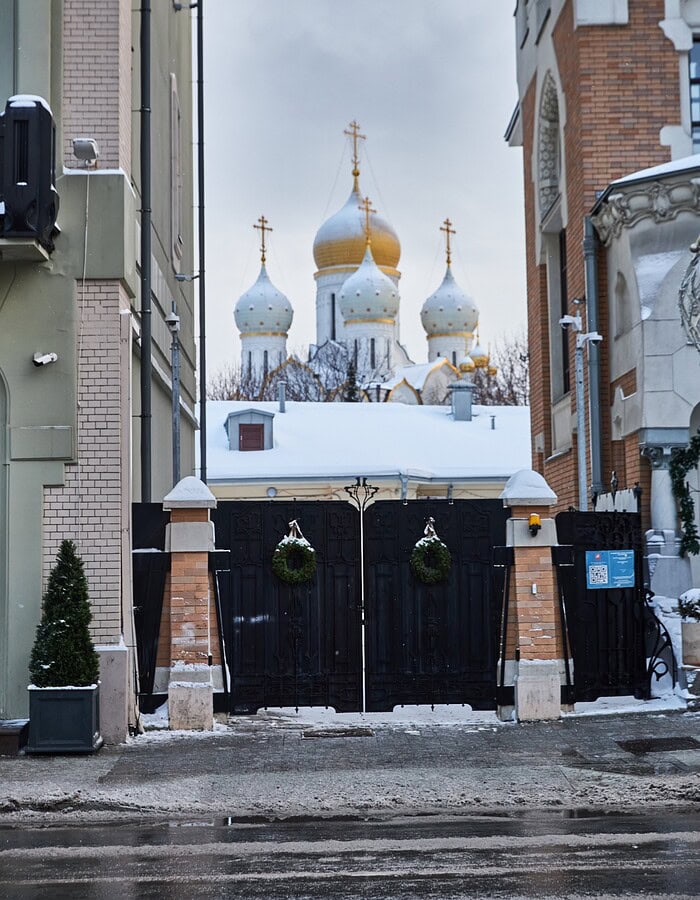 Gold and white church domes seen through a snowy Moscow street framed by buildings.