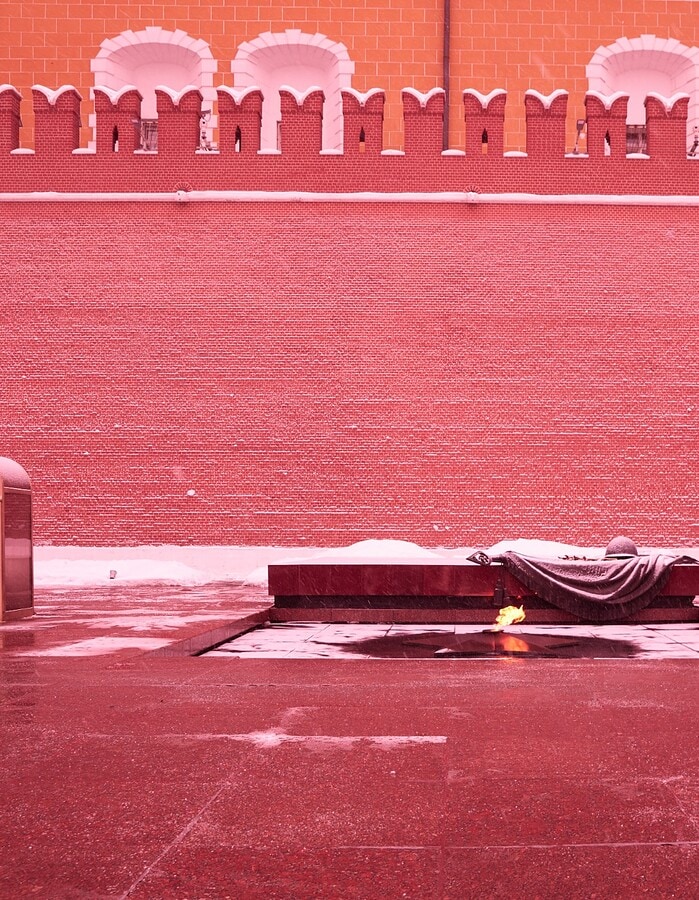 Snow falls over the Eternal Flame near the Kremlin wall in Moscow with guards standing in glass booths.