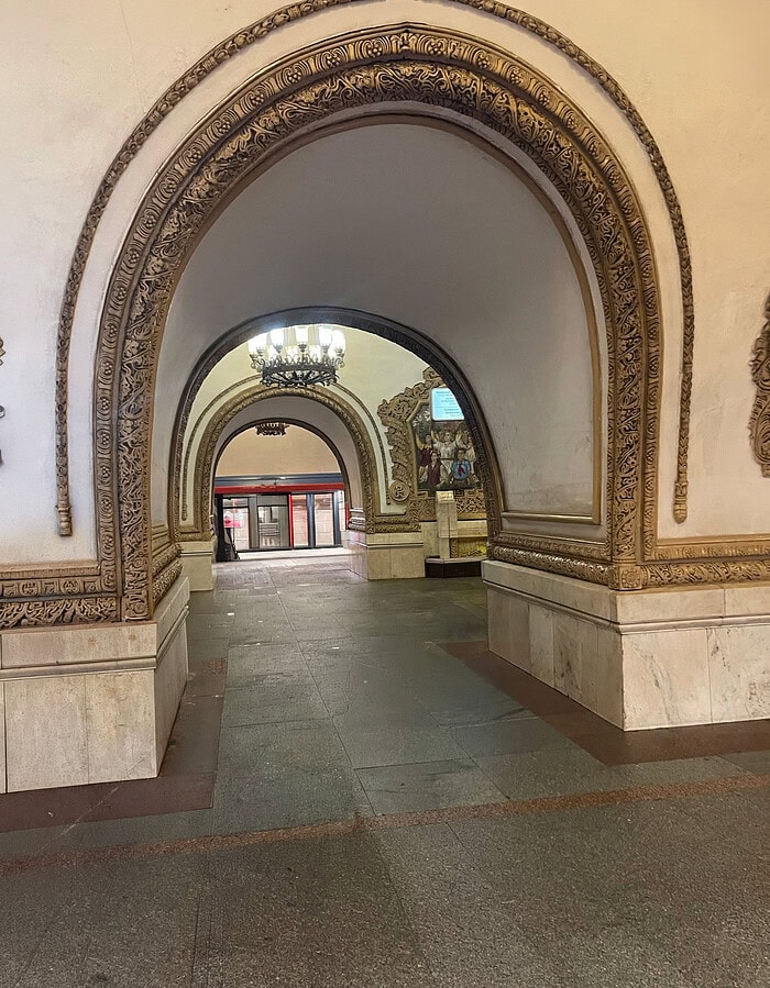 Ornate Moscow metro station interior with repeated arches, chandeliers, and carved architectural details.