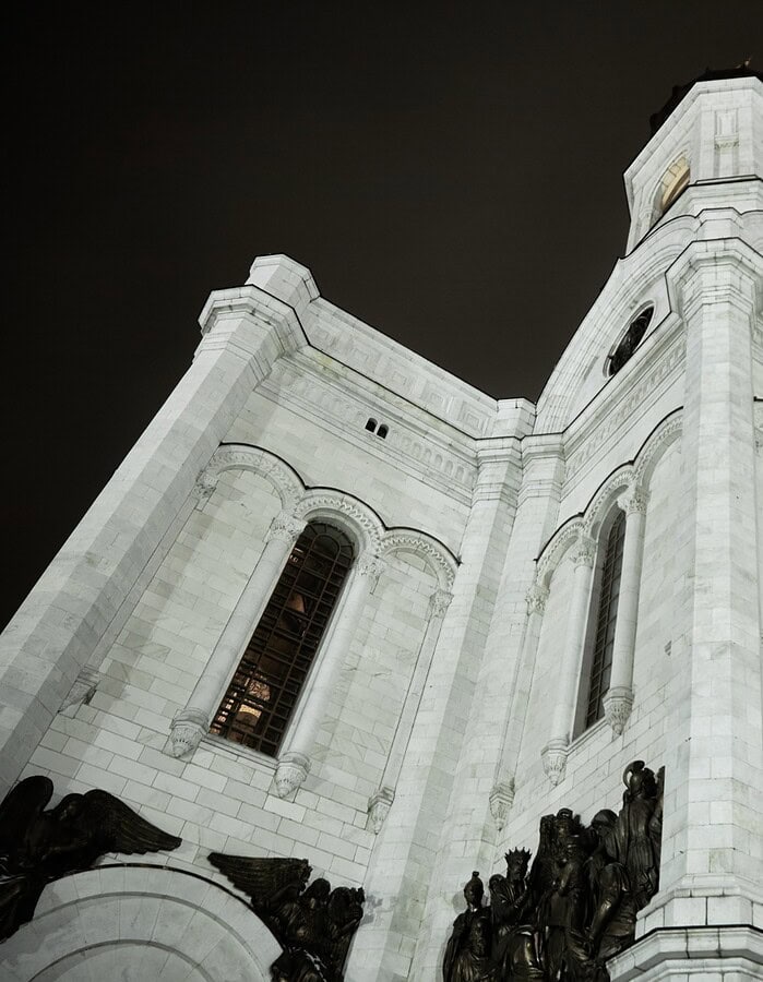 Low angle night view of a white Moscow cathedral with sculptural bronze reliefs.