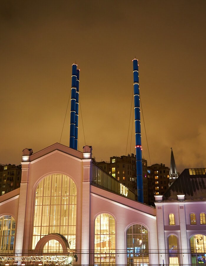Illuminated Moscow building with twin blue smokestacks under an amber winter night sky.