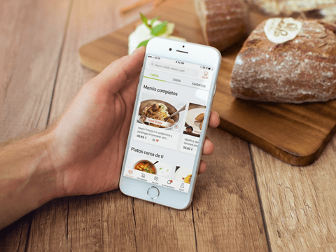 Mano que aguanta un móvil con una aplicación de comida en la pantalla.